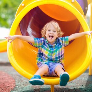 young boy smiling at the bottom of a yellow slide